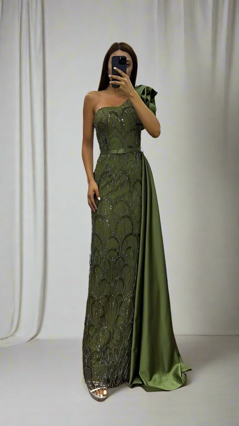 Woman wearing a green evening gown taking a mirror selfie indoors.